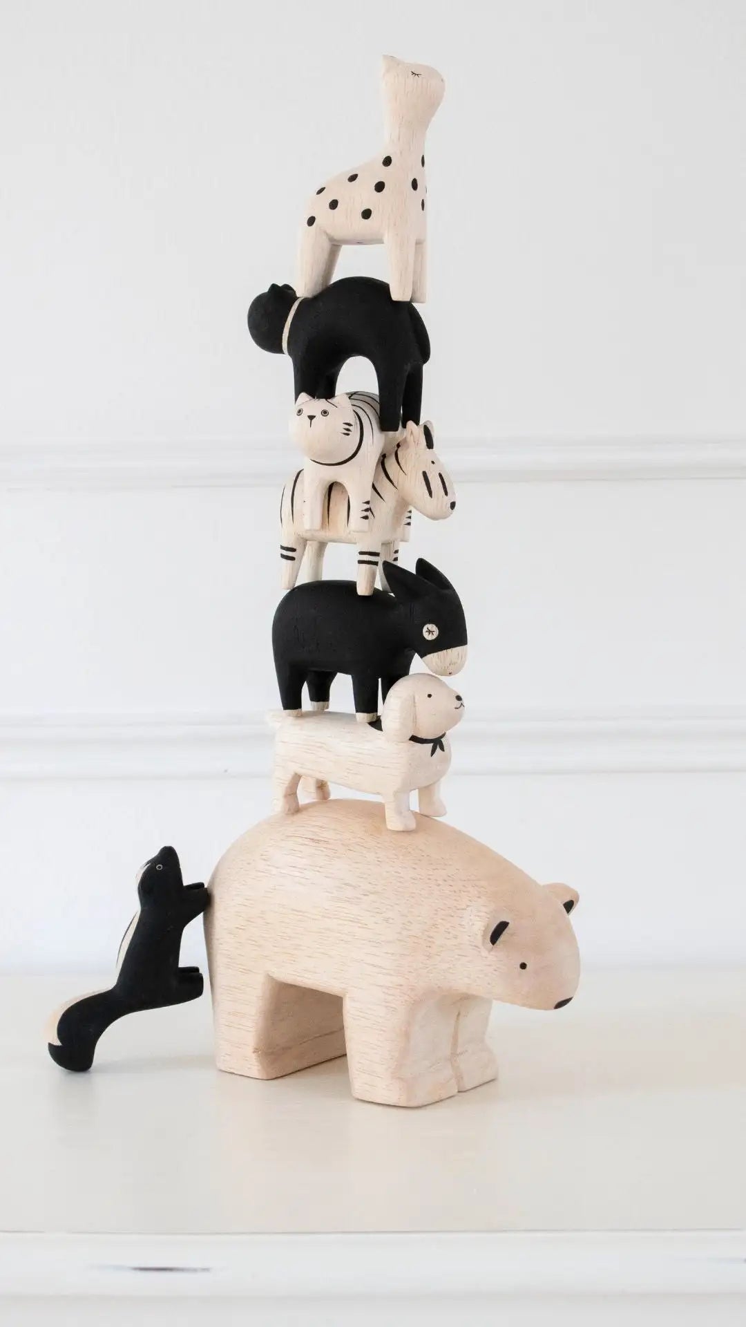 Une charmante pile de figurines animales en bois artisanales, présentant une base d'ours polaire avec des animaux noirs et crème, incluant des chats tachetés, des zèbres, des chiens et des girafes dans des poses ludiques.