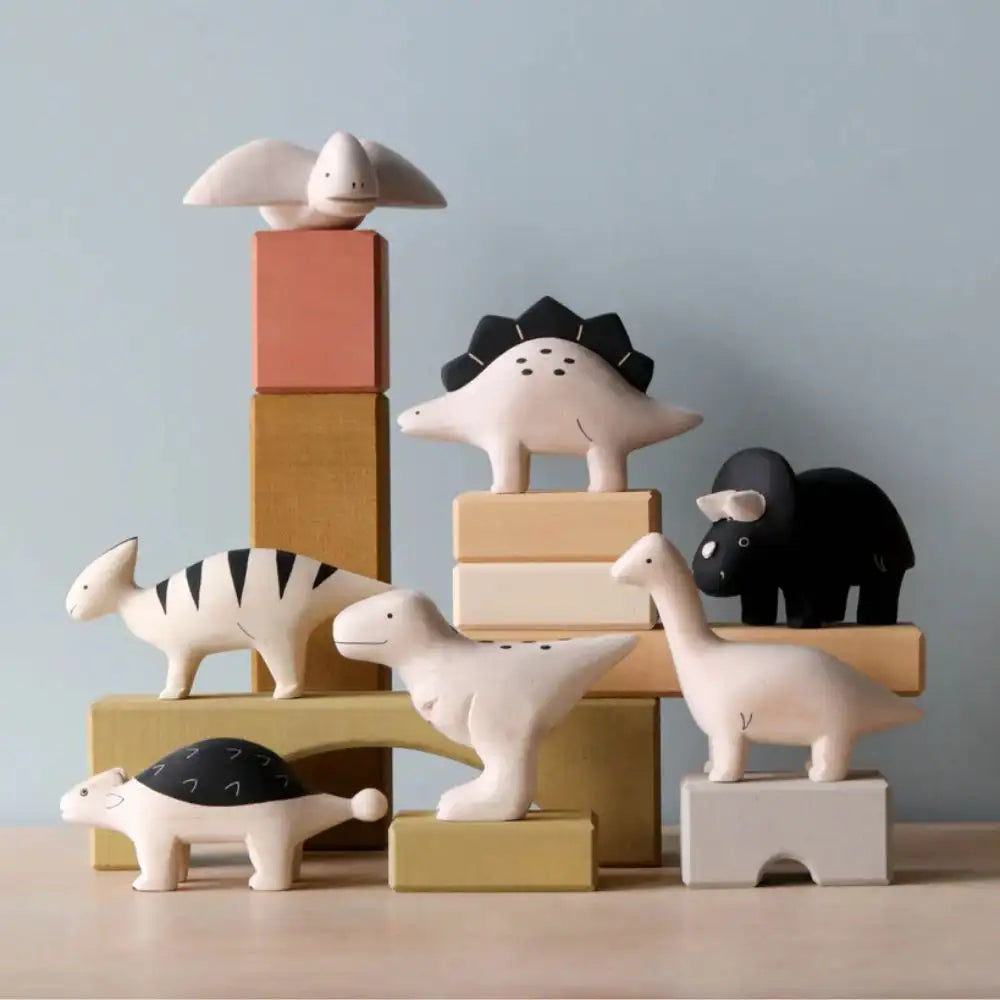 Une collection de figurines de dinosaures en bois minimalistes aux tons pastel doux et noir, chacune avec des détails peints simples.
